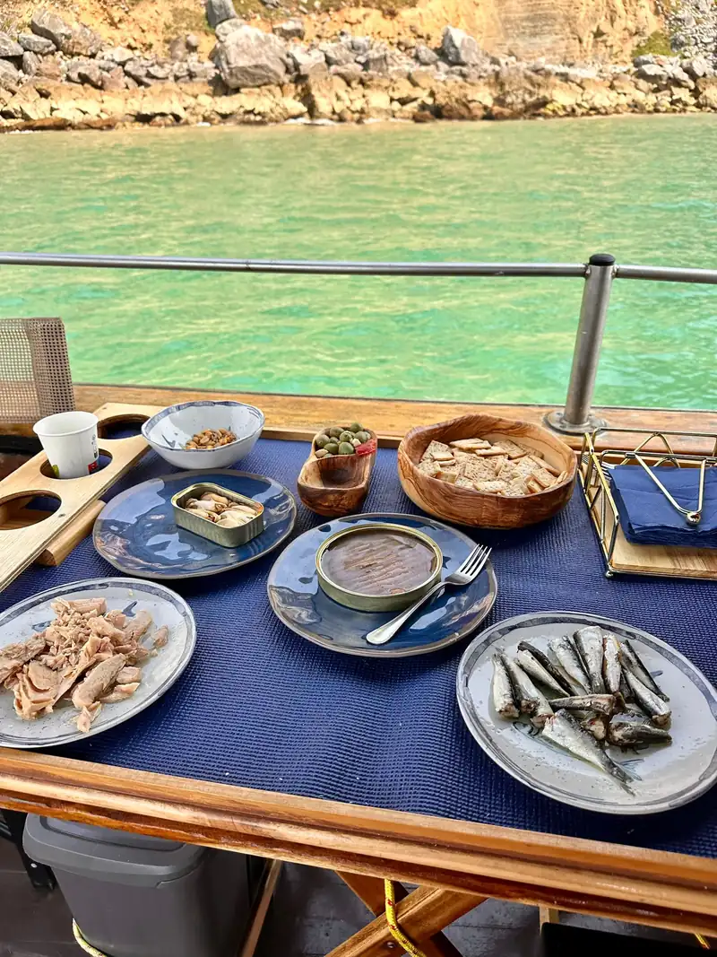 Mesa de degustación en cubierta con platos de conservas y el acantilado al fondo