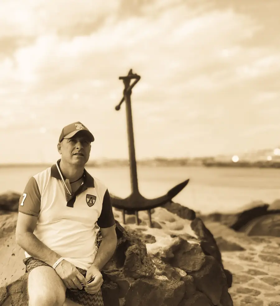 Retrato en sepia del patrón junto a un ancla, a la orilla del mar
